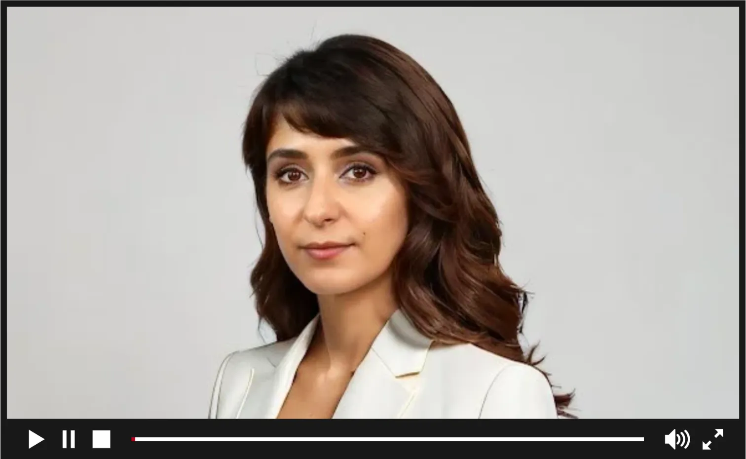 A career coach and trainer in a white suit and white blouse. The background is a gray wall.
